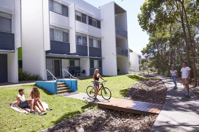 Students relaxing on grass and biking near building exterior at Griffith University Village Gold Coast in Gold Coast Student Accommodation