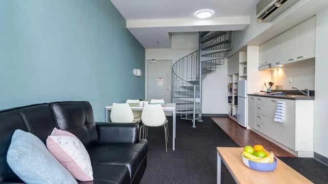 Black leather couch dining table spiral staircase kitchen living room at UniLodge @ Metro Adelaide in Adelaide Student Accommodation