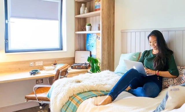 Woman on bed with laptop study desk Bedroom at Canvas The Parade in Cardiff Student Accommodation
