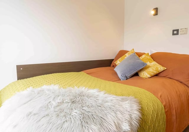Bed with orange bedding yellow and faux fur throws bedroom at iQ Astor House in Plymouth Student Accommodation