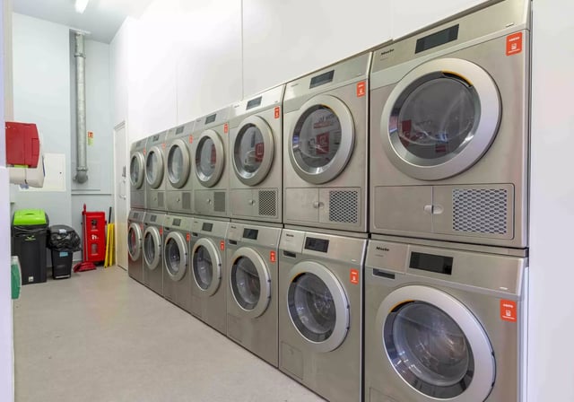 Stacked laundry machines and bins communal area laundry room at iQ Astor House in Plymouth Student Accommodation