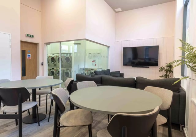 Round tables chairs sofas laundry room television communal area at iQ Astor House in Plymouth Student Accommodation