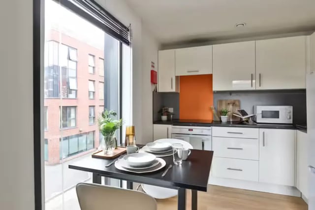 Table chairs microwave white cabinets orange splashback kitchen at Maple House in Liverpool Student Accommodation