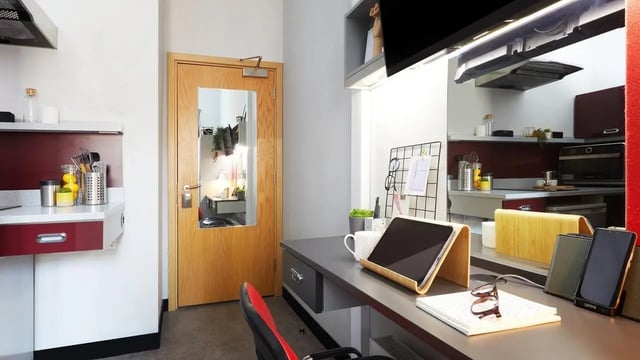 Desk with tablet and chair and kitchen area at Pillar Box in Coventry Student Accommodation