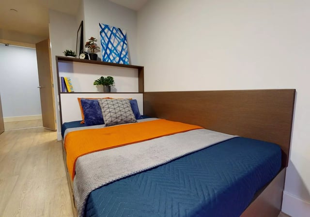 Bed with orange throw pillows artwork bedroom at iQ Penworks House in Birmingham Student Accommodation