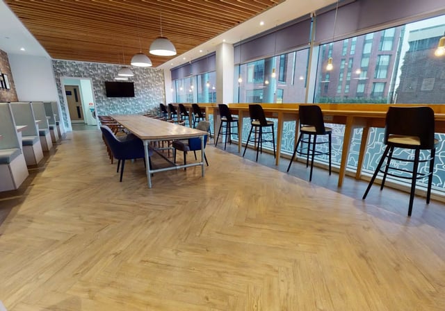 Long table blue chairs bar stools large windows common area at iQ Penworks House in Birmingham Student Accommodation