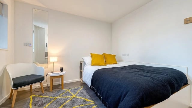 Bed with yellow pillows and dark blue blanket bedroom at Collegiate Merlin Heights in Leicester Student Accommodation