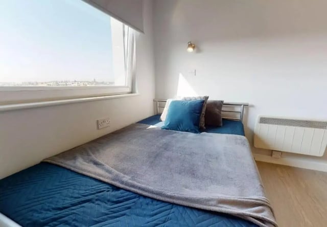 Bed with blue bedding grey throw two pillows bedroom at iQ Marsden House in Leeds Student Accommodation
