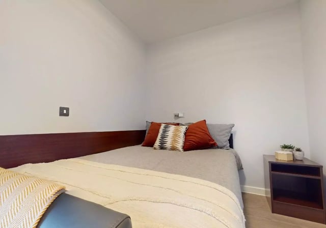 Bed with decorative pillows and side table bedroom at iQ Highbury in London Student Accommodation