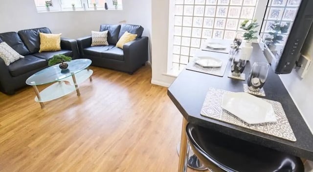 Black leather sofas glass coffee table dining area living room at Manchester House in Manchester Student Accommodation