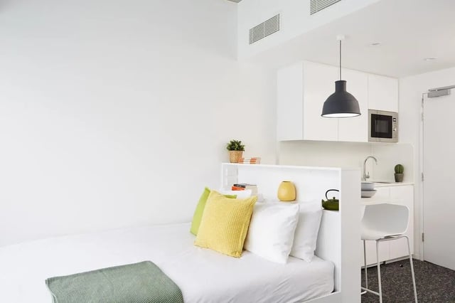 Bed pillows kitchen counter microwave white chair studio apartment at Scape Carlton in Melbourne Student Accommodation