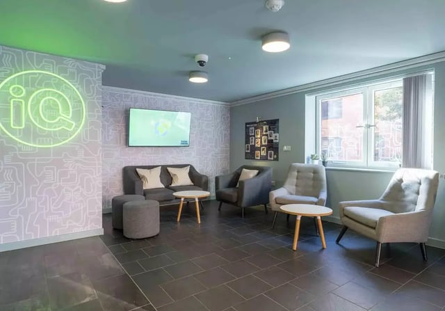 Comfortable seating area with TV and neon logo living area at iQ Leeds in Leeds Student Accommodation