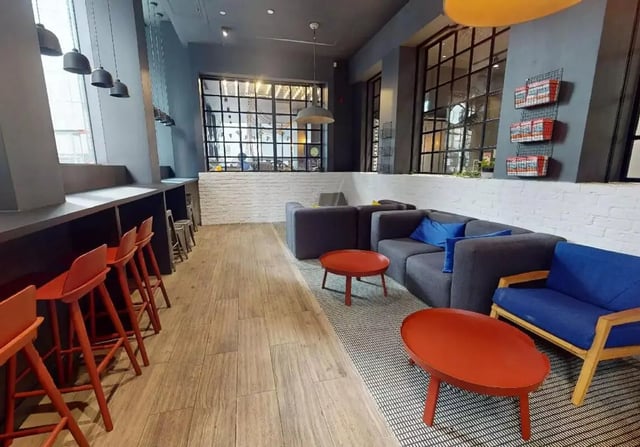 Modern lounge seating with orange stools and gray sofas Living room at iQ Shoreditch in London Student Accommodation