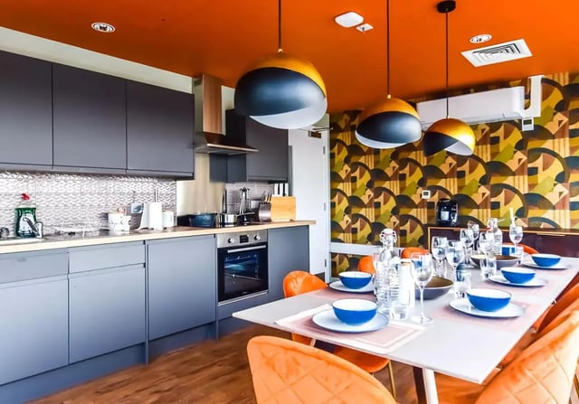 Modern grey cabinets dining table with place settings and orange chairs kitchen at iQ Bloomsbury in London Student Accommodation