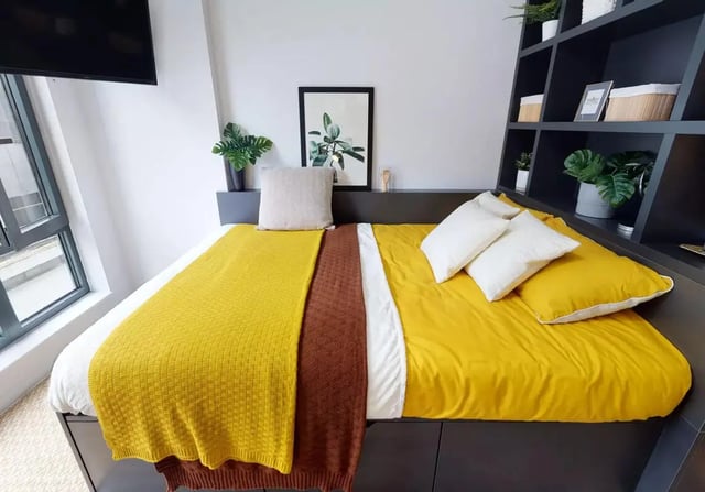 Bed with yellow blanket white pillows plants bedroom at iQ Bloomsbury in London Student Accommodation