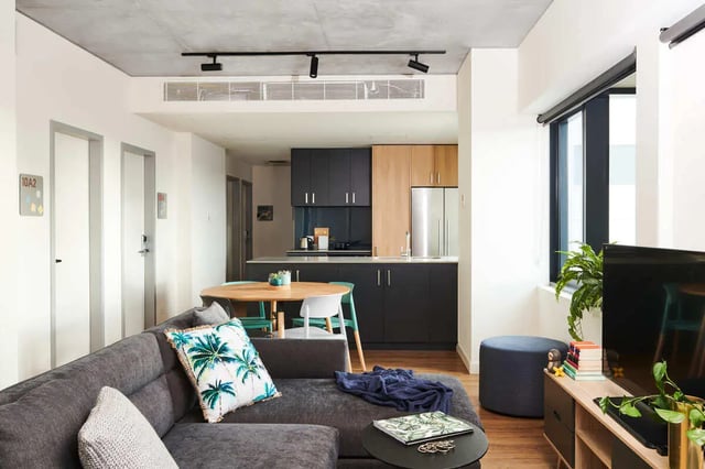 Gray sectional sofa with palm print pillow living room at Scape Uni Square in Melbourne Student Accommodation