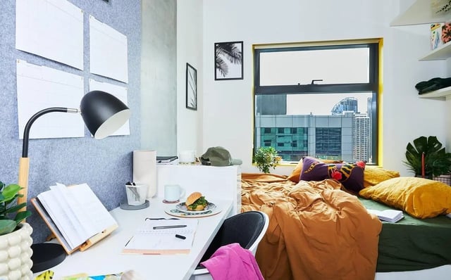 Desk with lamp, bed with pillows, cityscape view bedroom at Scape Franklin in Melbourne Student Accommodation