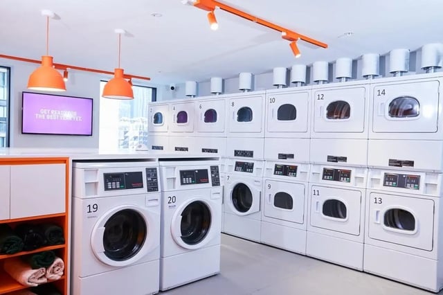 Row of stacked white laundry machines with orange accents Laundry room at Scape Franklin in Melbourne Student Accommodation
