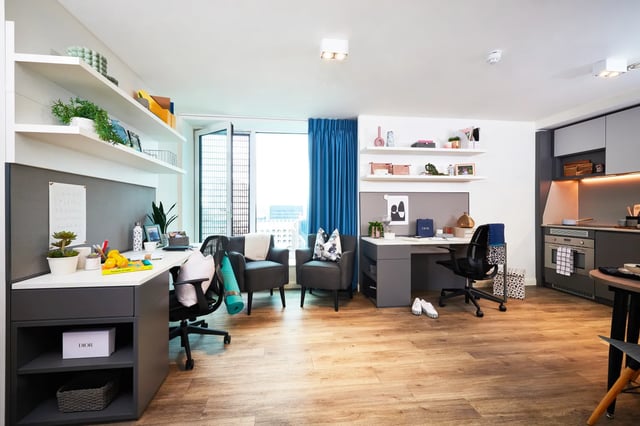 Two desks chairs plants and kitchen area living room at Vita Student Manchester Circle Square in Manchester Student Accommodation