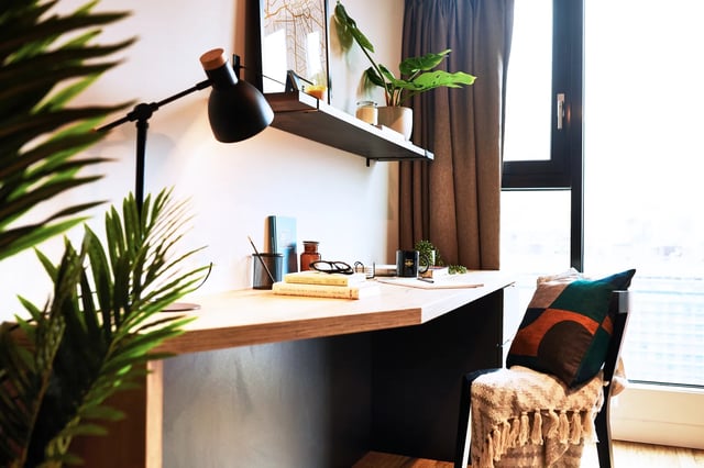 Desk with books plant lamp chair study area at Vita Student Manchester Circle Square in Manchester Student Accommodation