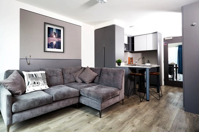 Grey sofa kitchen counter with stools living room at Vita Student Newcastle Strawberry Place in Newcastle Upon Tyne Student Accommodation