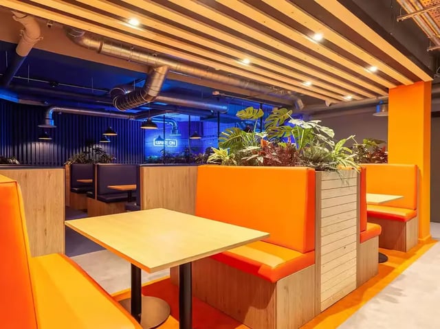 Orange booths wood tables plants dining area at The Bridge Guildford in Guildford Student Accommodation