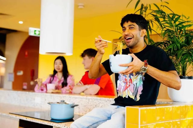 Young man eating noodles with friends kitchen at Scape Kingsford in Sydney Student Accommodation