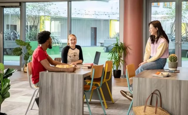 People studying at communal table with courtyard view common area at Emily Bowes Court in London Student Accommodation