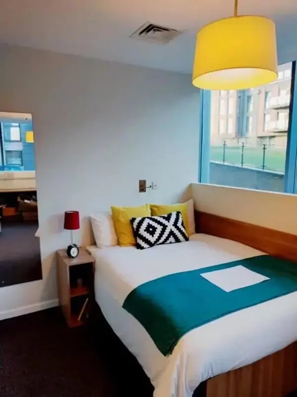Bed with teal throw pillows and lamp bedroom at Emily Bowes Court in London Student Accommodation