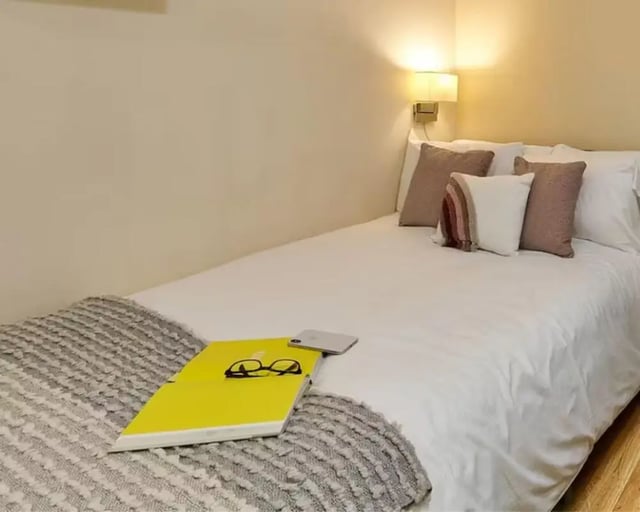 Bed with pillows phone book glasses bedroom at The Hub in London Student Accommodation