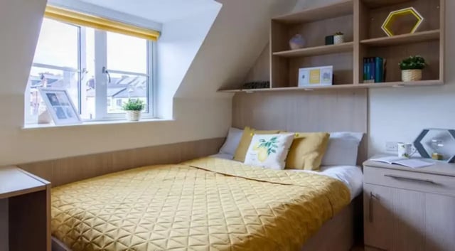 Bed with yellow quilt shelves with decor Bedroom at Iron Bridge Studios in Exeter Student Accommodation