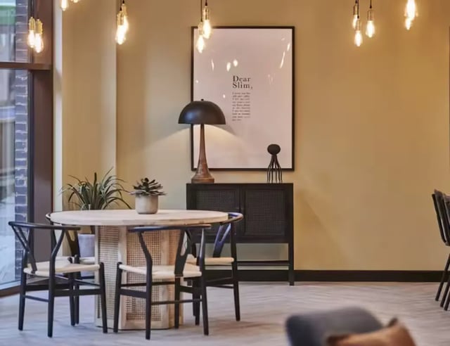 Round table chairs plants framed art cabinet living room at York House in Nottingham Student Accommodation