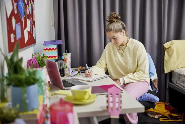 Student writing at desk with laptop and bed study area at Boundary x Scape in Sydney Student Accommodation
