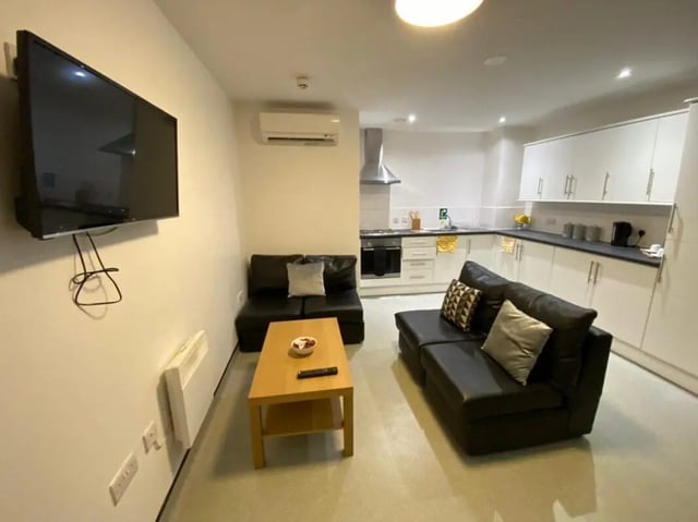 Living room with sofas kitchen area and TV living room at Longside House Bradford in Bradford Student Accommodation