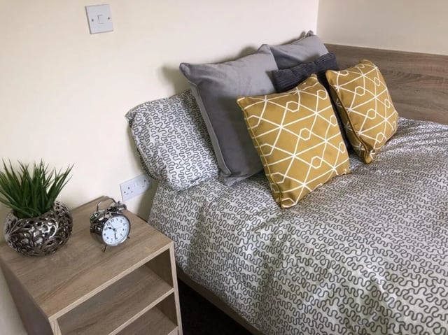 Bed with patterned duvet grey and yellow pillows bedside table bedroom at Jubilee Court in Preston Student Accommodation