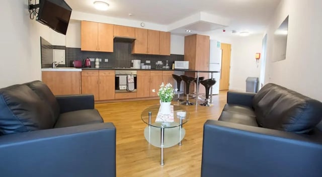Two black sofas round glass table and kitchen living room at Exeter One in Exeter Student Accommodation