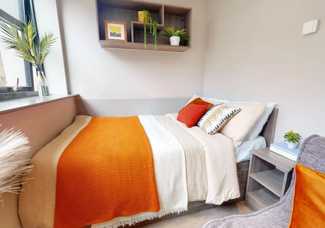 Bed with orange throw pillows and shelf Bedroom at Waterlane House in Bristol Student Accommodation