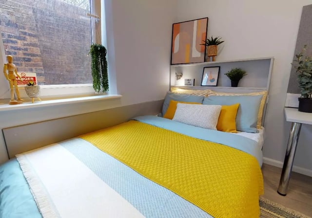 Bed with yellow blanket plants and artwork bedroom at iQ Will Wyatt Court in London Student Accommodation