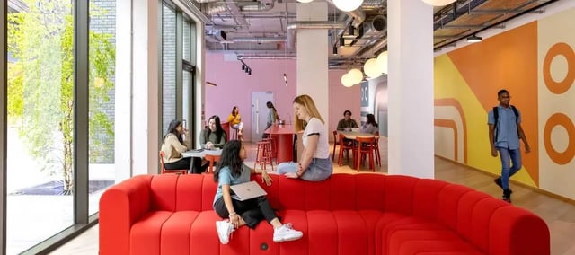 Students relaxing on red sofa with laptops communal area. at Scape Mile End Canalside in London Student Accommodation