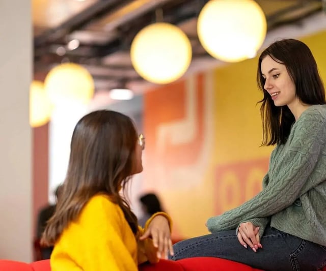Two students talking on red couch living room at Scape Mile End Canalside in London Student Accommodation