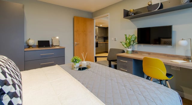 Bed desk television and kitchen visible bedroom at Symons House in Leeds Student Accommodation