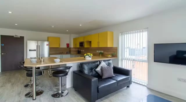 Kitchen island with stools black sofa and TV living area at Dover Street Apartments in Leicester Student Accommodation