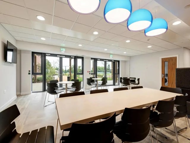 Large table chairs and blue pendant lights common area at Cricket Field Court in Exeter Student Accommodation