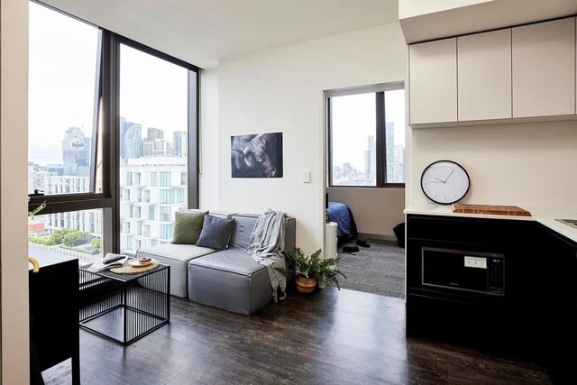 Sofa with cushions by window and kitchen area living room at Scape Queensberry in Melbourne Student Accommodation