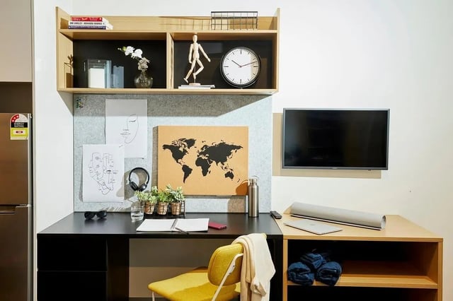 Desk with art headphones clock TV laptop and chair study area at Scape Queensberry in Melbourne Student Accommodation