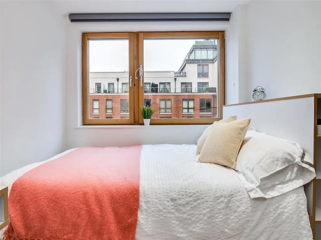Bed with coral throw pillows and window bedroom at New Orient House in London Student Accommodation