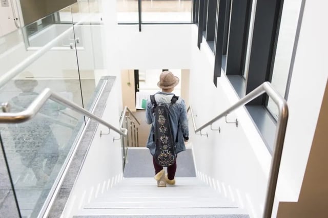 Person with musical instrument case walks down stairs Interior at Prince Consort Village in London Student Accommodation
