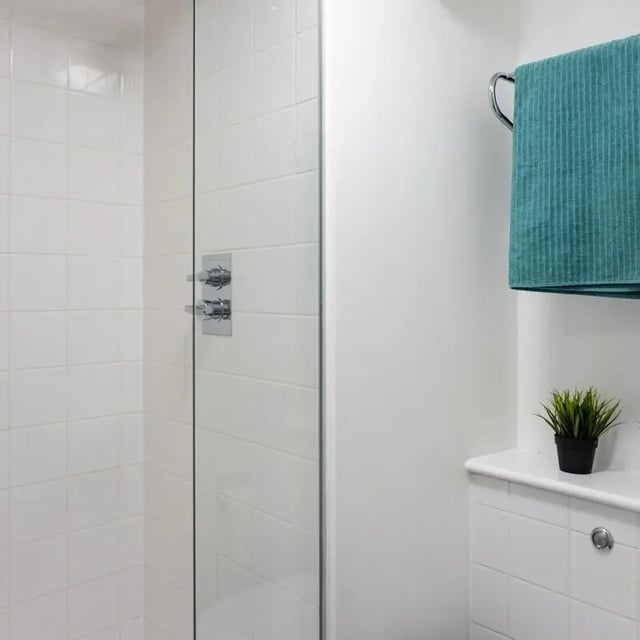 Shower tiles glass door chrome taps towel plant bathroom at Prince Consort Village in London Student Accommodation