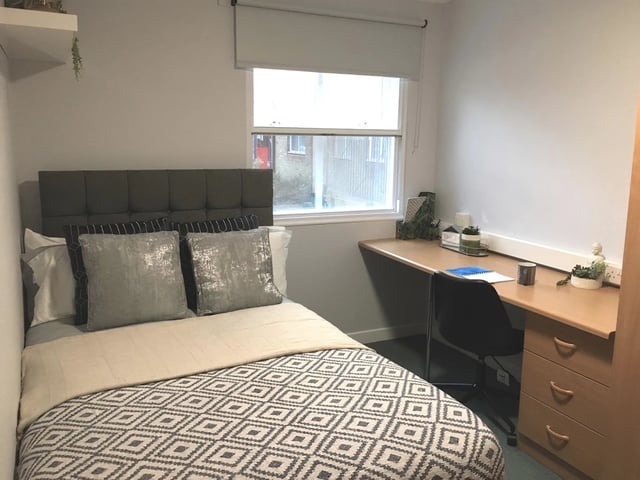 Bed with patterned duvet and desk study area bedroom at Dean House in London Student Accommodation