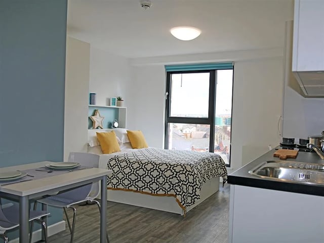 Bed yellow pillows patterned duvet desk kitchen studio apartment at Botanic Studios in Belfast Student Accommodation